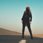 woman in black jacket and pants standing on gray sand during daytime