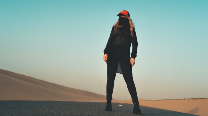woman in black jacket and pants standing on gray sand during daytime